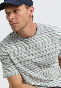 T-shirt rayé à col rond dans des couleurs claires avec des rayures bleu et vert variées. Manches courtes, en coton, avec une texture douce.