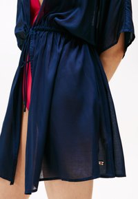 Kimonou din chiffon de culoare bleumarin, cu talie elastică, mâneci scurte și deschidere pe lateral, având un mic accent cu brand pe tiv.
