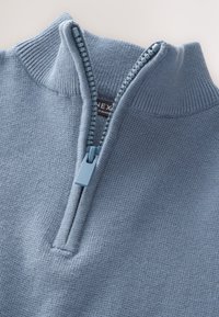 Svetlomodrý sveter so štvrťzipsom, so žíhaným golierom, hladkým materiálom a kontrastným plastovým zipsom. Vo vnútri viditeľná visačka.