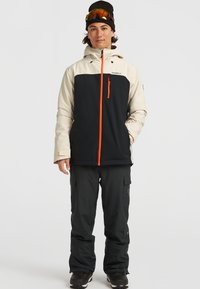 Herrarnas snöjacka i krämfärg och svart, med blixtlås fram och orange detaljer, en huva och elastiska muddar. I kombination med svarta cargobyxor.