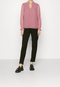 Blusa rosa trasparente con motivo testurizzato e colletto arricciato, abbinata a pantaloni neri tapered e mocassini neri lucidi.