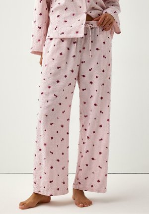 Løse lyserøde pyjamasbukser med lille rød blomsterprint båret barfodet, kombineret med matchende top med knapper og lange ærmer.