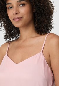 Camisola di raso rosa con scollatura a V, spalline sottili e texture liscia. Il tessuto ha una finitura leggermente lucida.