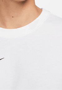Bílé bavlněné tričko s kulatým výstřihem a černým logem Nike na levé straně, hladká textura a standardní střih.