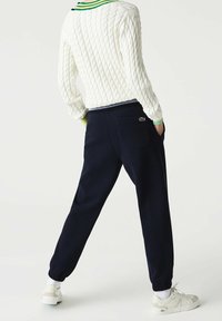 Vit kabelstickad tröja med gröna och blå accenter, i kombination med marinblå joggerbyxor med bakficka och elastiska muddar, bärs tillsammans med vita sneakers.