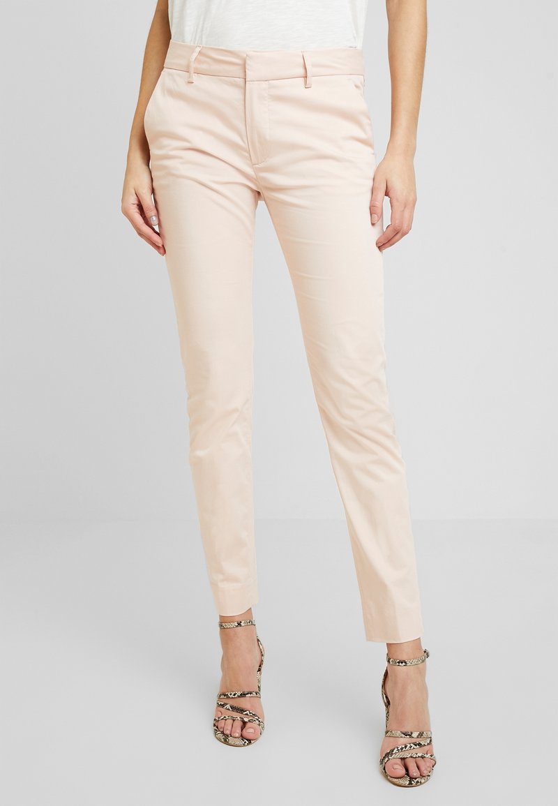 Pantalons ajustés rose clair avec une coupe slim, devant plat et brillant subtil, associés à des talons métalliques à imprimé serpent et à lanières.