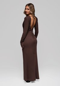Abito brown a maniche lunghe con profondo scollo aperto sulla schiena, silhouette aderente e lacci regolabili sul retro. Tessuto morbido e liscio con texture minima.