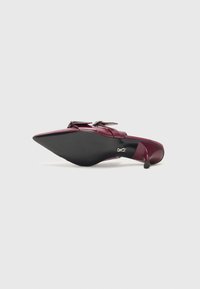 Pantof cu toc înalt burgundy, cu vârf ascuțit, finisaj lucios din paten, accente decorative cu cataramă și talpă texturată neagră.