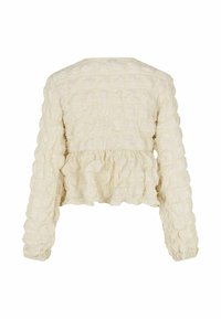 Peplum blúzka v off-white textilnom materiáli. Má dlhé rukávy, zhrnutý spodný lem a jemné volániky. Skračený strih.