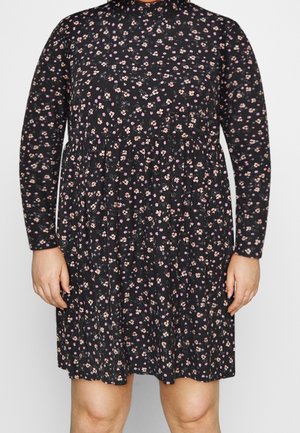 Zwarte jurk met lange mouwen en een klein roze en wit bloemenpatroon, met een getailleerde taille, gedragen door een persoon die van nek tot knieën te zien is.