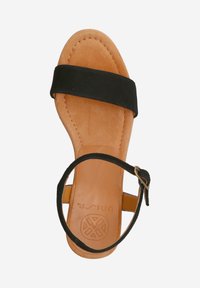 Black suede sandal with a tan leather insole, flat sole, adjustable ankle strap, and circular logo detail on the bottom.