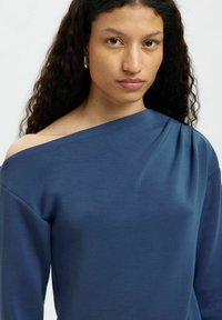 Blaues Off-Shoulder-Oberteil aus weichem Stoff, mit Drapierungen auf einer Seite und langen Ärmeln. Glatte Textur mit lockerer Passform.