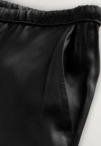 Sort satinstof med en elastisk talje med rynker, udstyret med en sidelomme og en glat tekstur. Finpudsede syninger er synlige.