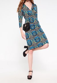Blue and black patterned dress with a V-neck, ¾ sleeves, and a fitted silhouette. Paired with black platform sandals and a small handbag.
