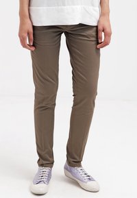 Brune slim-fit bukser lavet af glat stof, parret med lyslilla sneakers med en tekstureret overdel og hvid sål.