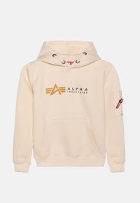 Hoodie color crema con cappuccio regolabile, tasca frontale e tasca con zip sulla manica. Presenta un logo e dettagli in oro e nero "ALPHA INDUSTRIES".
