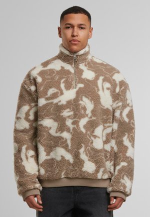 Beige Fleece-Pullover mit weißem Hasenmuster und Viertelreißverschluss. Mit hohem Kragen und elastischen Bündchen. Weiches, strukturiertes Material.