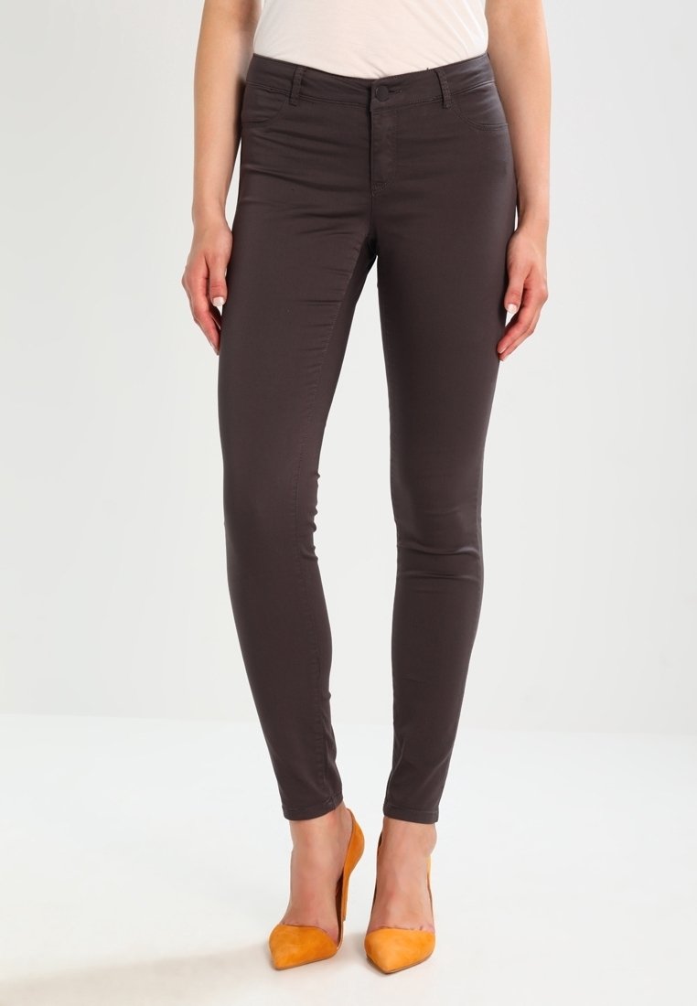 Tmavě hnědé slim-fit kalhoty vyrobené z hladkého materiálu, s klasickým středním pasem a pěti kapsami, doplněné žlutými podpatky.