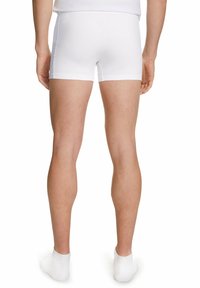 Shorts in cotone bianco, design aderente, lunghezza a metà coscia, bordi senza cuciture e texture morbida. Indossati con calzini bianchi alla caviglia.
