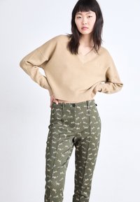 Beige cropped trui met een V-hals en ribbelzoom, gecombineerd met groene broek met een tijgerpatroon en een voorste knoopsluiting.