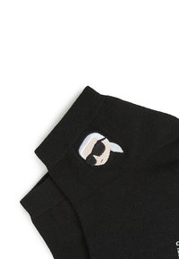 Calcetines negros con un gráfico tejido de una figura con gafas de sol y cabello blanco en el puño, fabricados con material suave y elástico.