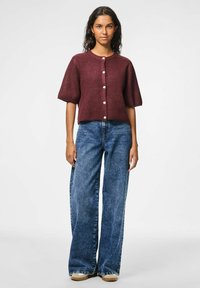 Bordeaux gebreide cropped cardigan met korte mouwen, voorzien van een ronde halslijn en vijf witte knopen. Gecombineerd met high-waisted wijdvallende blauwe jeans.