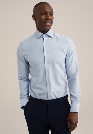 Lichtblauwe blouse met lange mouwen, knoopsluiting aan de voorkant, kraag, gladde katoenen stof, gecombineerd met donkerblauwe broek. Standaard manchetten en een aansluitende snit.