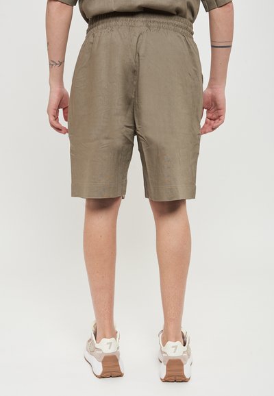 Pantaloni corti khaki con elastico in vita, realizzati in un tessuto leggero e liscio, con un taglio dritto, abbinati a sneaker di colore chiaro.