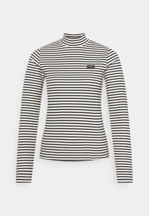 Camisa de manga larga con cuello alto, rayas horizontales en blanco y negro, con un pequeño parche de logotipo rectangular en el pecho izquierdo.