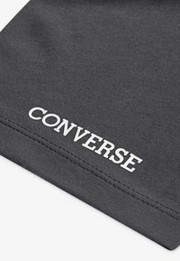 Šedá látka s logem "CONVERSE" v bílé barvě, výrazně umístěným blízko dolního okraje, se hladkým povrchem a jemným prošitím.