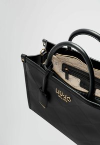 Borsa a tracolla nera trapuntata con doppio manico nero, accentata da dettagli in oro e foderata con un tessuto a motivi. Presenta una tasca con zip all'interno.