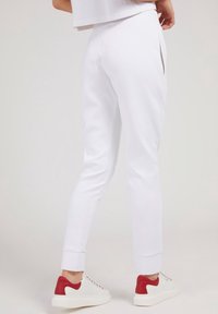 Białe dresowe spodnie o dopasowanym kroju, z bocznymi rozcięciami, ściągaczami na kostkach i gładkiego materiału, połączone z białymi i czerwonymi sportowymi półbutami.