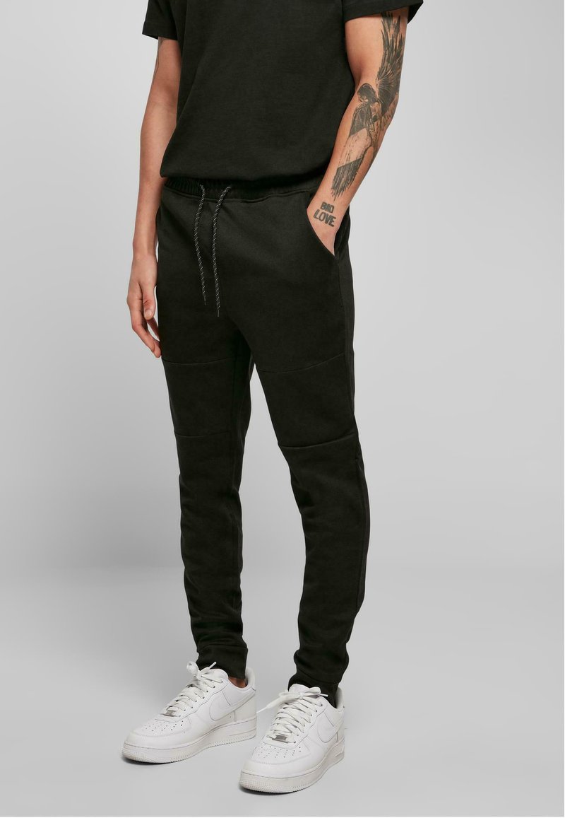 Pantalons de jogging noirs en tissu doux, avec une taille élastique à cordon de serrage, des poches latérales et des jambes effilées. Portés avec des baskets blanches.