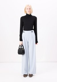Tunique à col roulé noir à manches longues, pantalon taille haute bleu clair à jambes larges avec deux boutons sur les côtés, sac à main noir texturé et chaussures à imprimé animal.