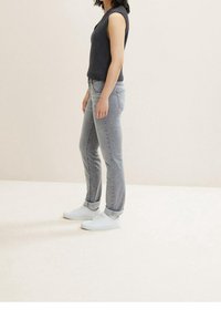 Jeans de denim gris claro con los puños enrollados, combinados con zapatillas blancas. El corte es recto, con un ligero desgaste y un diseño clásico de cinco bolsillos.