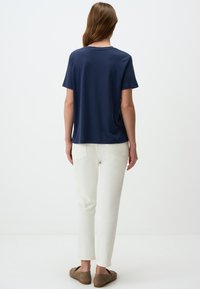 Navyblauwe t-shirt met korte mouwen en een relaxte fit, gecombineerd met witte slim-fit broek en bruine instappers, gezien vanuit de achterkant.