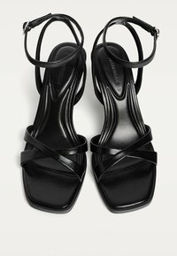 Schwarze, hochhackige Sandalen mit glänzender Oberfläche, quadratischen Zehen und mehreren schlanken Riemen. Mit einem verstellbaren Knöchelriemen für sicheren Halt.
