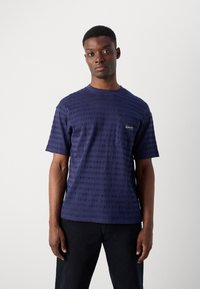 T-shirt bleu marine à manches courtes avec des rayures texturées et une petite poche sur la poitrine gauche arborant un logo de marque. Fabriqué à partir d'un tissu doux.