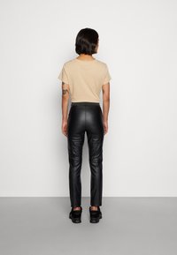 Camiseta de algodão bege, com mangas curtas, combinada com calças de couro pretas slim-fit. Textura suave e design ajustado.