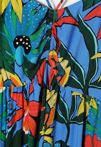 Lebhaftes blaues Kleid mit floralem Muster, das rote, gelbe und grüne Akzente aufweist. Glatte Stoffqualität, geraffte Details und fließende Silhouette.