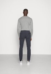 Grå långärmad skjorta, mörka rutiga byxor med bakfickor och vita sneakers. Enkelt mönster, figurnära passform och subtil färgkontrast.