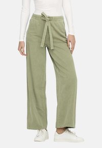 Pantalons larges vert clair en coton doux, avec une ceinture à nouer et une coupe décontractée, associés à des baskets blanches.