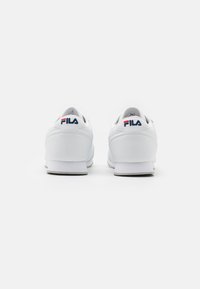 Hvite sneakers med en glatt læroverdel, polstret krage, og rød og blå FILA-logo på hælen; flat gummisåle, rund tå.
