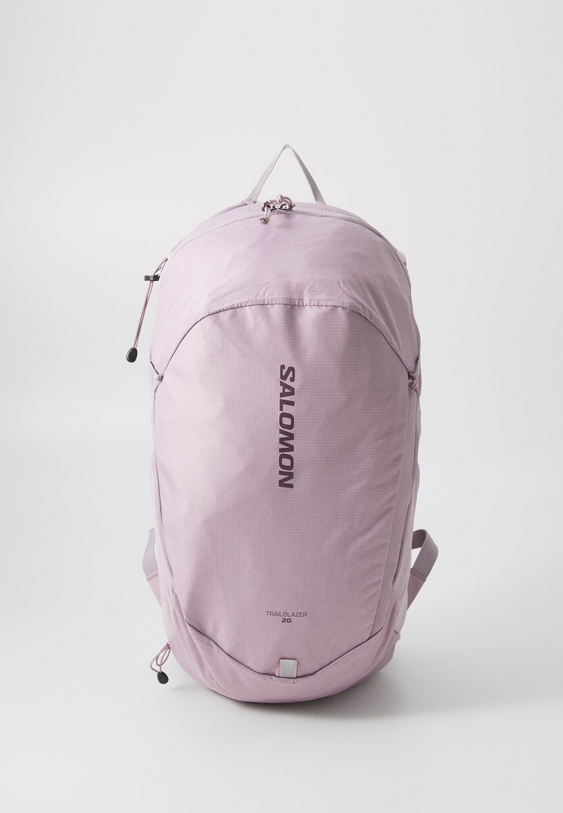 Sac à dos violet clair de forme arrondie, en tissu texturé, avec une fermeture éclair à l'avant et des bretelles ajustables ; présente les logos "SALOMON" et "TRAILBLAZER 20".