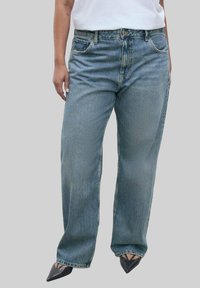 Jeans in denim azzurro chiaro con una vestibilità rilassata, leggermente sfilacciati, design a cinque tasche e vita alta, abbinati a scarpe nere con punta.