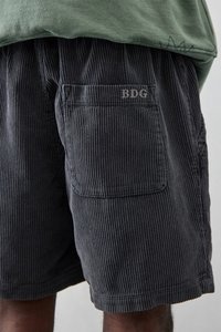 Mørkegrå betegnede shorts med strukturerede lodrette ribber, der har en baglomme og "BDG"-logoet broderet i lysegrå på lommen.