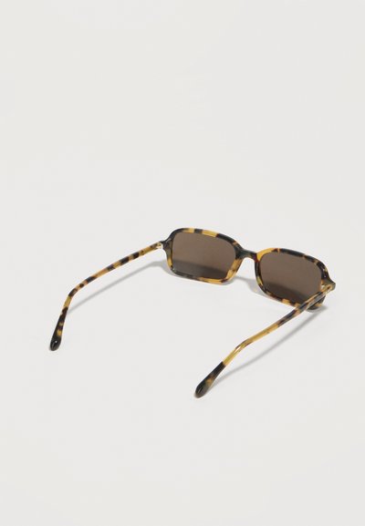 Ορθογώνια γυαλιά ηλίου με καμηλοπάρδαλη και σκουρόχρωμους φακούς, τοποθετημένα σε απλό ανοιχτό φόντο.