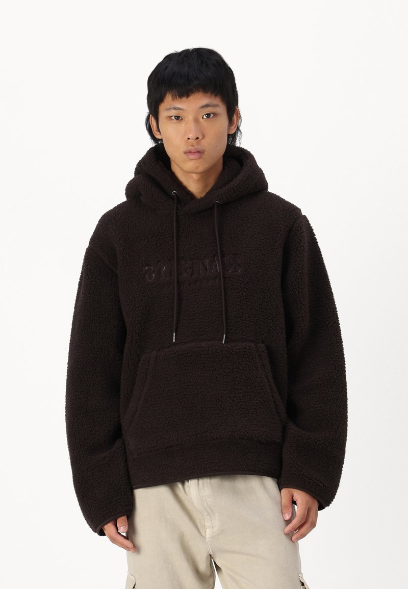 Hnědý fleecový hoodie s tkaničkami, měkkou texturou, přední kapsou a embosovaným logem "ORIGINALS". Volný střih a dlouhé rukávy.