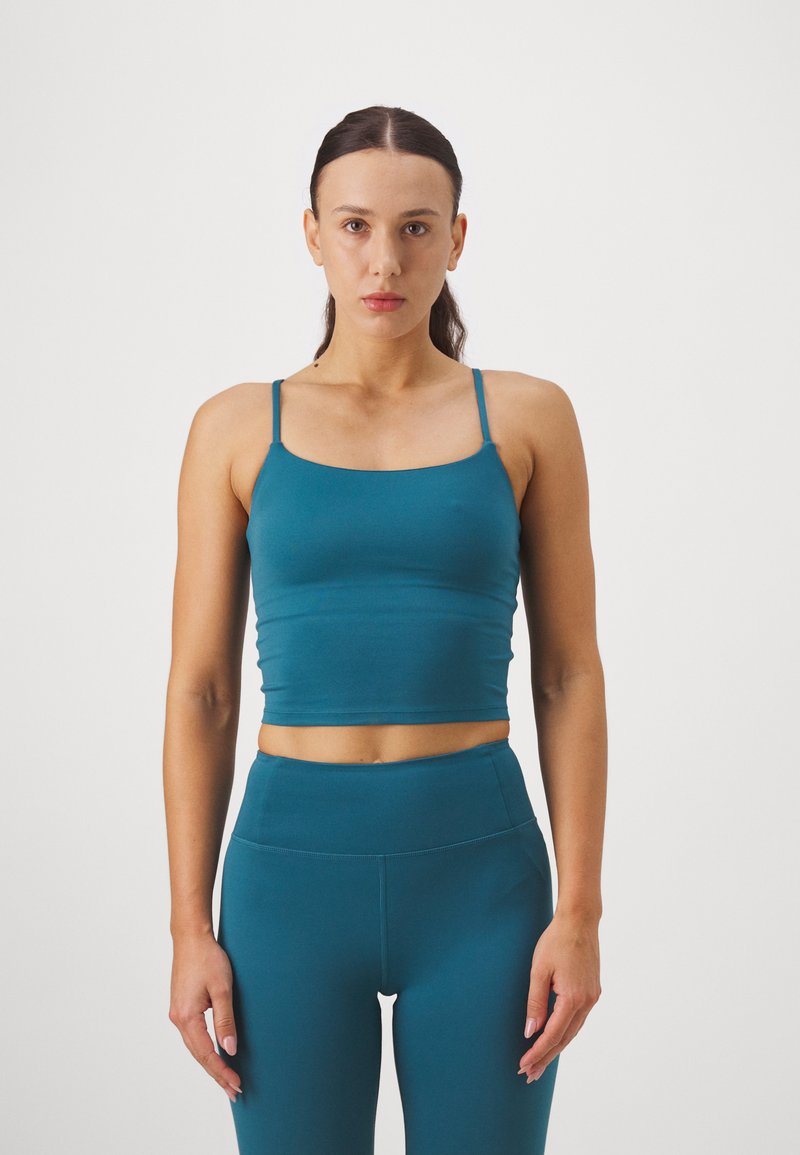 Teal uski crop majica s tankim naramenicama, izrađena od glatkog, rastezljivog materijala, uparen s hlačama visokog struka u boji koja se slaže.