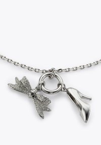 Srebrny naszyjnik z zawieszkami w kształcie kokardki i wysokich obcasów, ozdobionymi przezroczystymi kryształkami, zawieszony na łańcuszku ogniwowym.